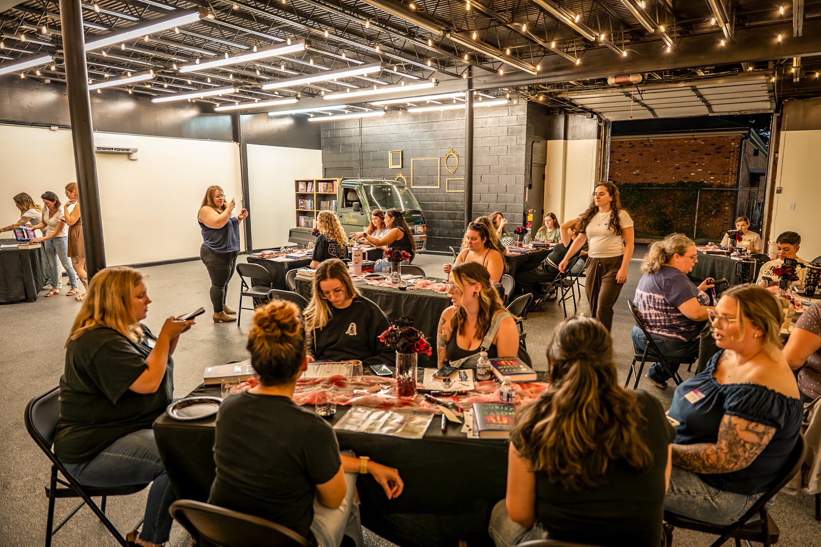 A Blush Club night in progress: members at black-clothed tables under strings of warm lights, the Blush Bus parked at the back of the room
