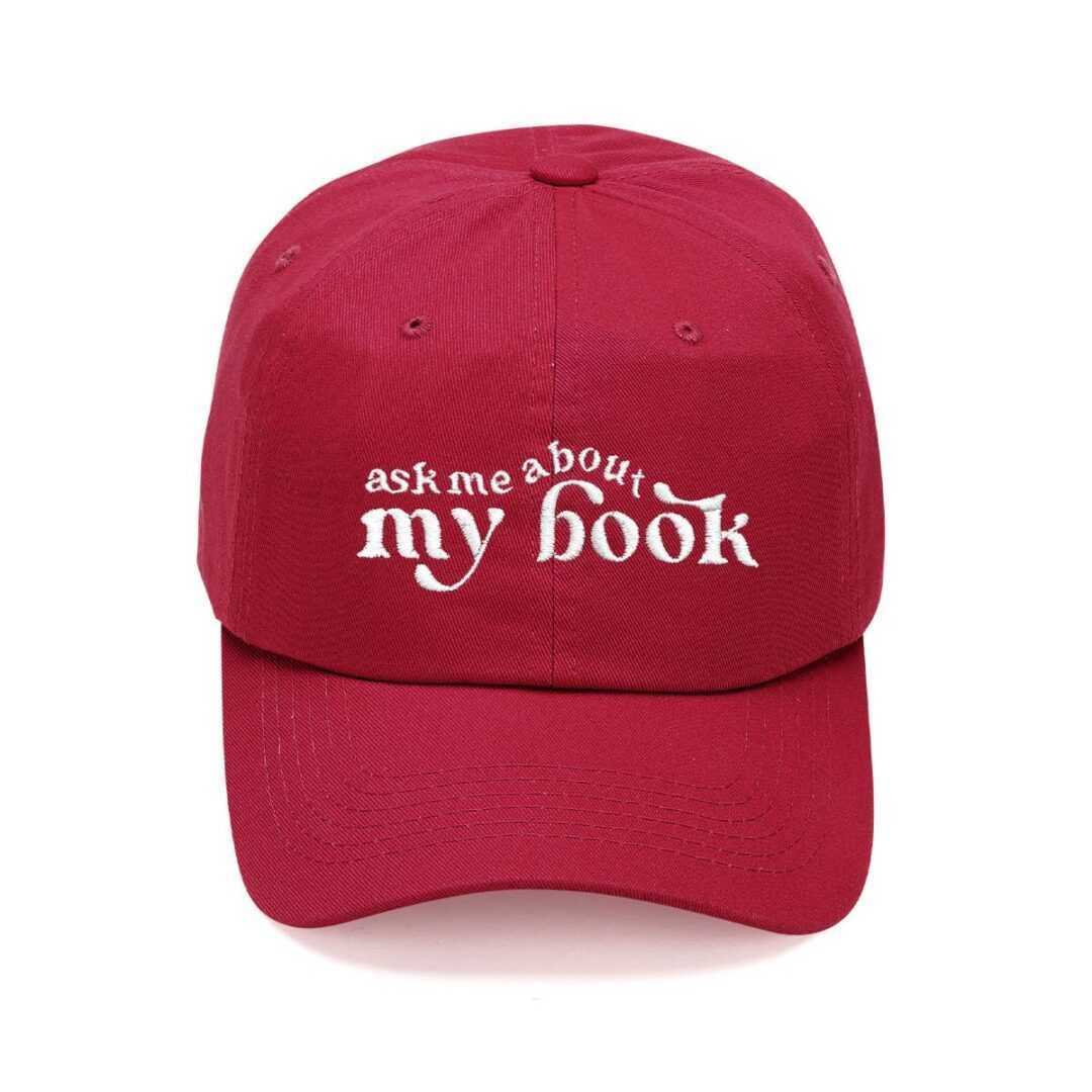 The Ask Me About My Book Cap is a red baseball cap embroidered with "ask me about my book" in white—ideal for fans of viral book recommendations and romance novels.