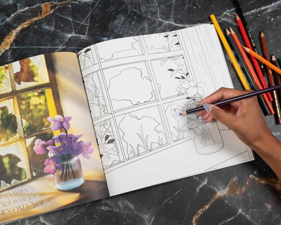 A hand colors flowers in Fourth Wing: The Official Coloring Book - by Entangled (Paperback), open to a window scene with a vase of flowers. Colored pencils and popular BookTok book inspirations sit nearby on the marble surface.