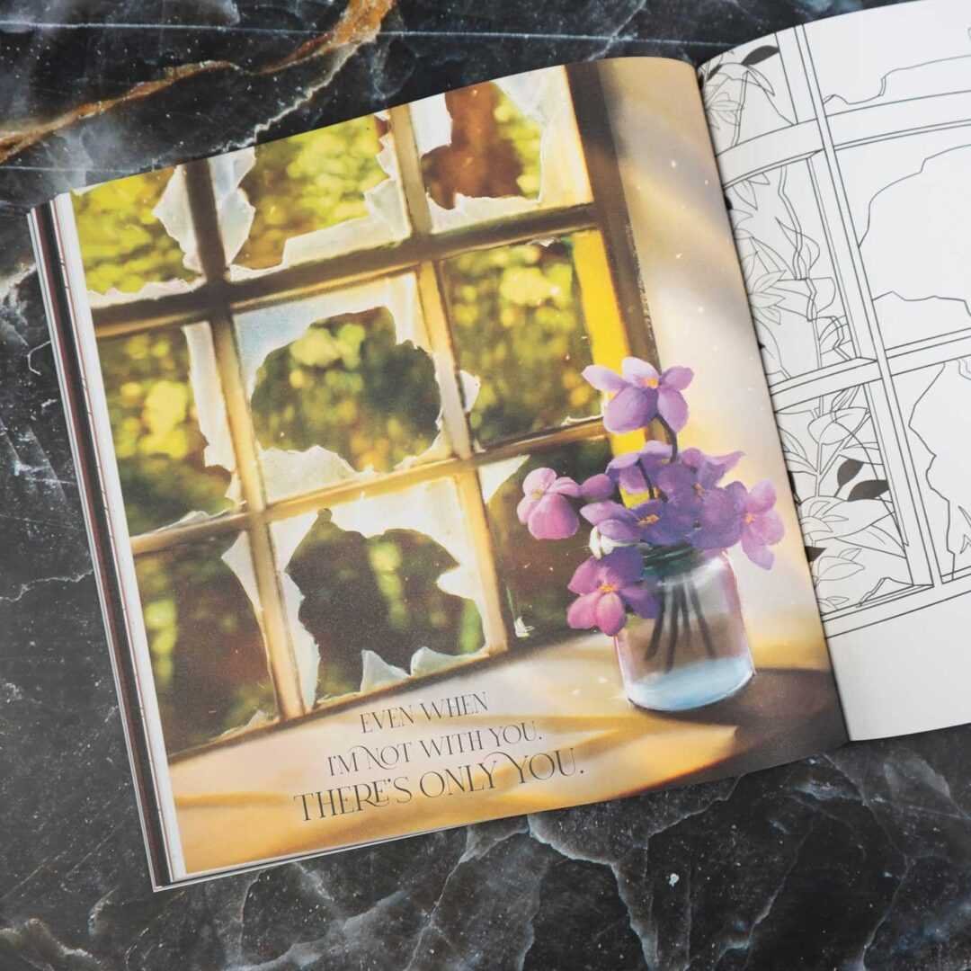 The Fourth Wing: The Official Coloring Book (Paperback by Entangled) is open on a dark marble surface, displaying a page with purple flowers on a windowsill and the text: "Even when I'm not with you, there's only you.