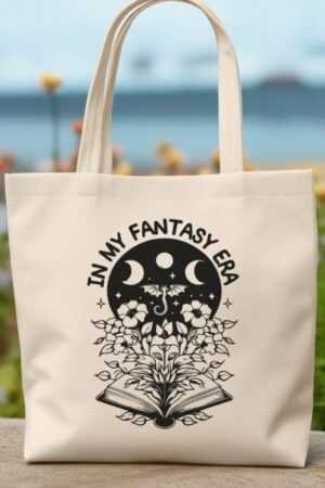 The In My Fantasy Era Reading Books Canvas Tote Bag features a beige design with an open book, blooming flowers, butterflies, moon phases, and IN MY FANTASY ERA text—ideal for carrying your favorite Romance Novels or trending BookTok reads.