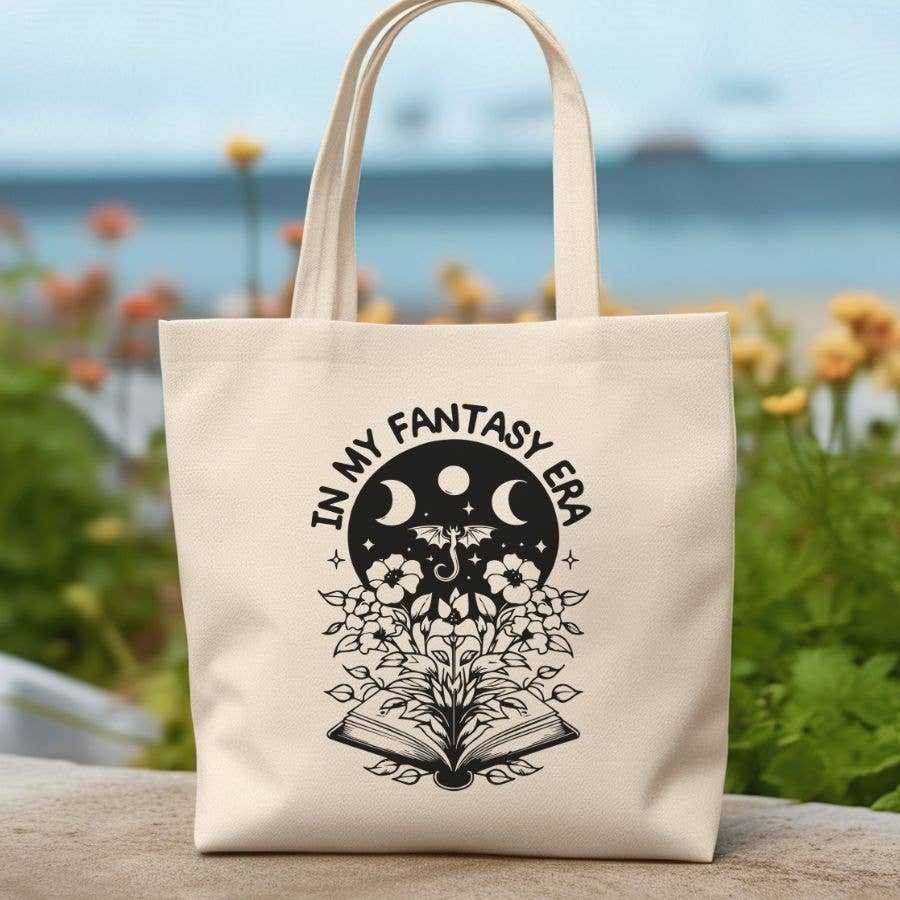 The In My Fantasy Era Reading Books Canvas Tote Bag features a beige design with an open book, blooming flowers, butterflies, moon phases, and IN MY FANTASY ERA text—ideal for carrying your favorite Romance Novels or trending BookTok reads.