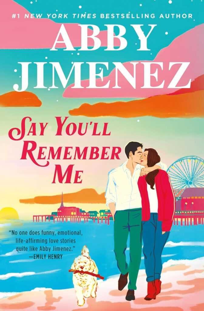 The cover of "Say You'll Remember Me" by Abby Jimenez features a vibrant illustration of a couple walking on the beach at sunset, the woman kissing the man’s cheek, while their dog walks ahead near a glowing pier and Ferris wheel.