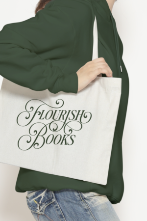 A person in a green hoodie and jeans holds the Flourish Tote, featuring ornate green script reading "Flourish Books," against a plain white background.