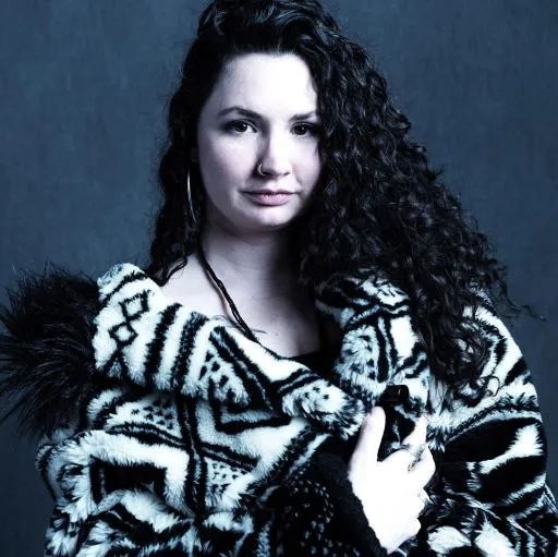 Channeling "My Demon Hunter: Deluxe Limited Edition – (Hell Bent) by Aurora Ascher," a woman with long, curly dark hair wears a fluffy black-and-white coat, hoop earrings, and a nose ring against a dark textured background.