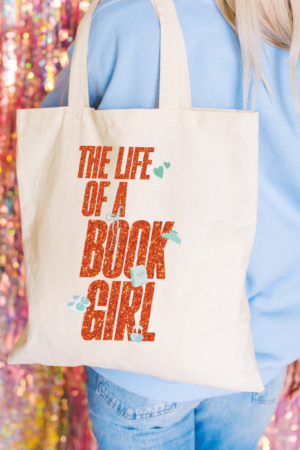 A person with long blonde hair holds the “Book store Tote Bag | Reader Gift | Life of a Book Girl,” featuring bold red lettering, making it an ideal gift for readers against a sparkly pink and gold background.