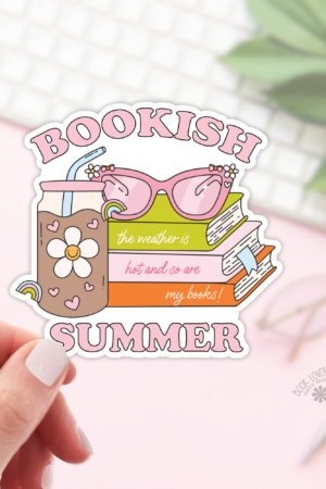 A hand holds a Bookish Summer Iced Coffee Sticker, showing pink sunglasses, a floral iced drink, and pastel books with the text: “Bookish summer. The weather is hot, and so are my books!” A plant and keyboard blur in the background.
