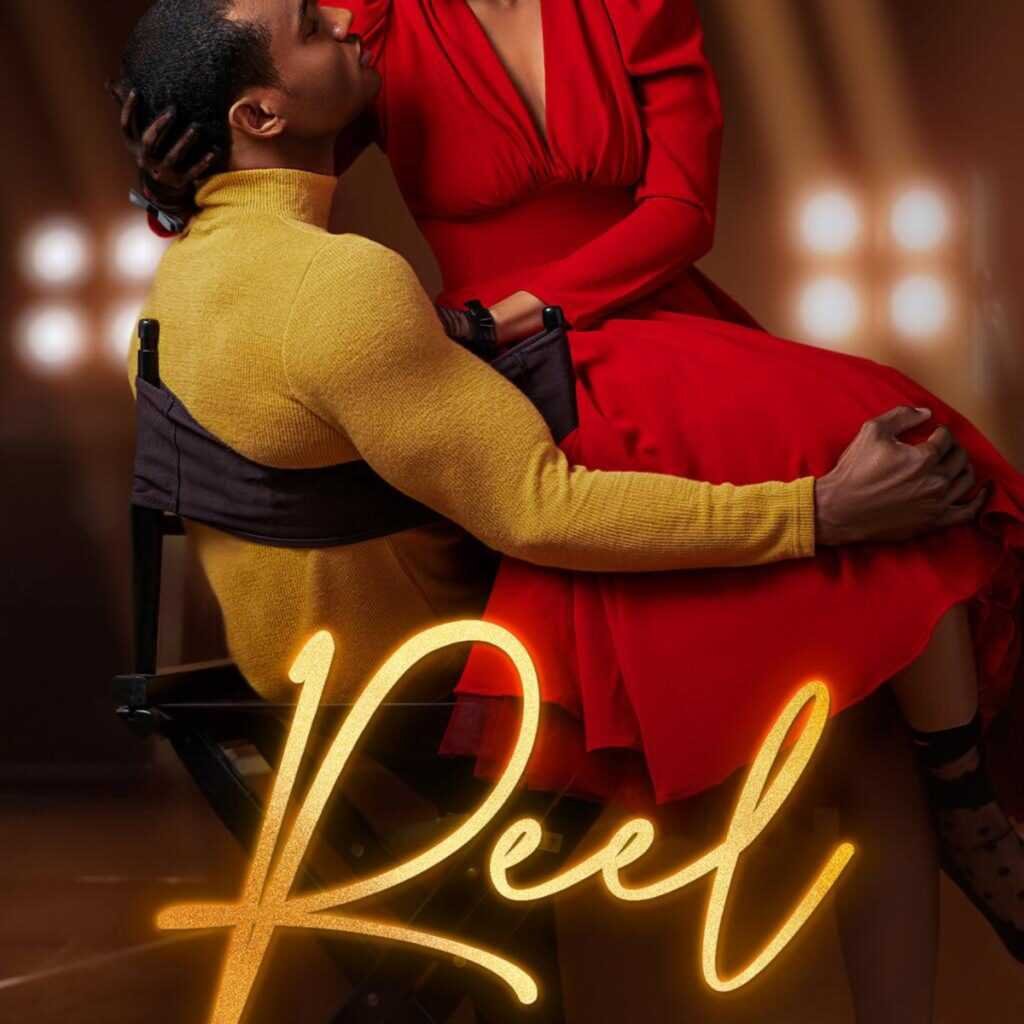 A man in a yellow sweater sits on a director’s chair with a woman in a red dress on his lap, softly lit under stage lights. "Reel - (Hollywood Renaissance) by Kennedy Ryan (Paperback)" glows at the bottom of the scene.